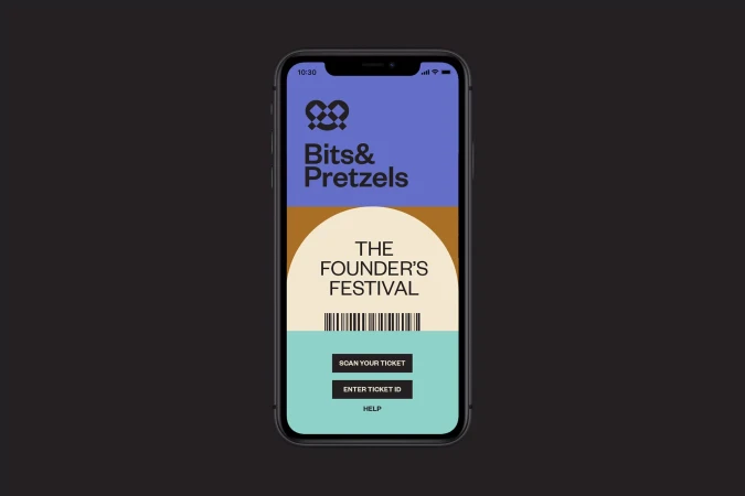 Mockup of smartphone displaying Bits & Pretzels app ticket with barcode on blue, brown, and cream interface, against dark grey backdrop.