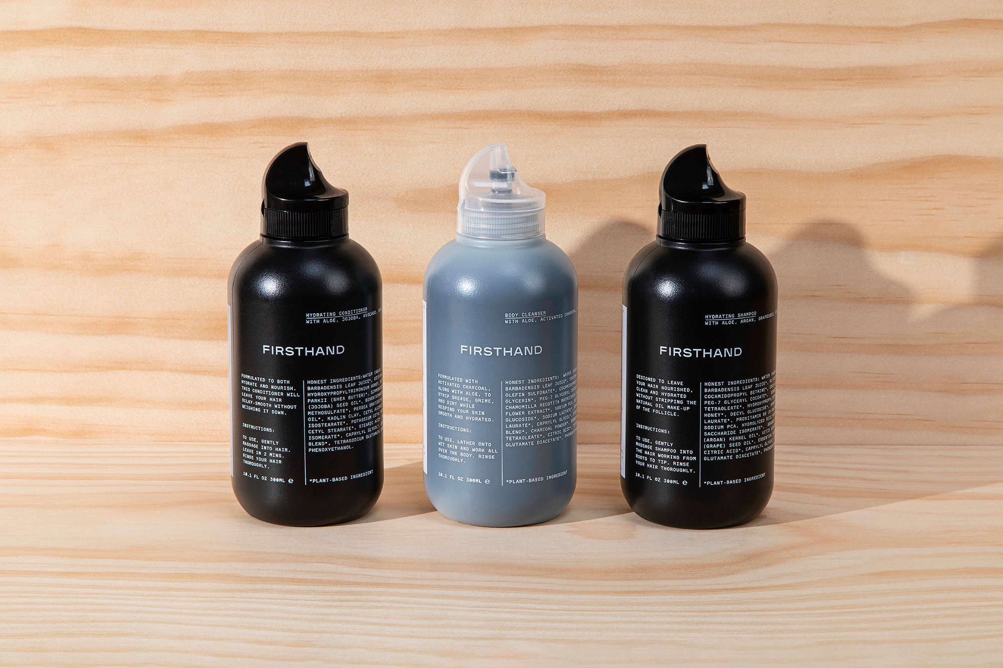 Three bottles of Firsthand hydrating shampoo and body cleanser, arranged on a light wood surface, showcasing minimalist product design.