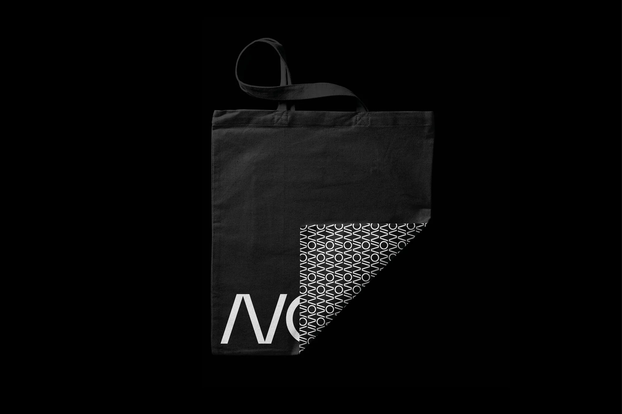 Black tote bag with white logo on a dark background. The reusable shopping bag has handles and folded patterned section.