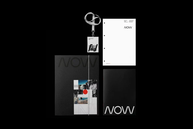 Flat lay of black and white 'NOW' branded marketing materials including a lanyard, notebook, letterhead, and booklet on black backdrop.