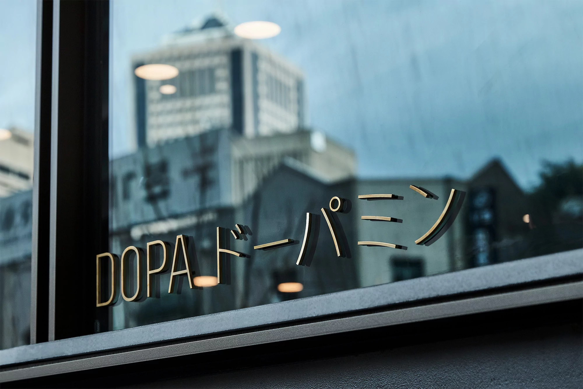 A close-up of a window with 'DOPA' and Japanese text, reflecting an out-of-focus city building, creating depth and urban ambiance.