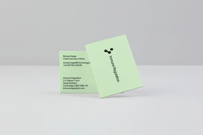 Two light-green business cards, one upright and one angled, display company and contact information on a light grey surface.