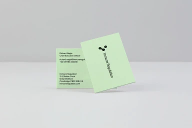 Two light green business cards with black typography displayed on a pale grey studio surface.