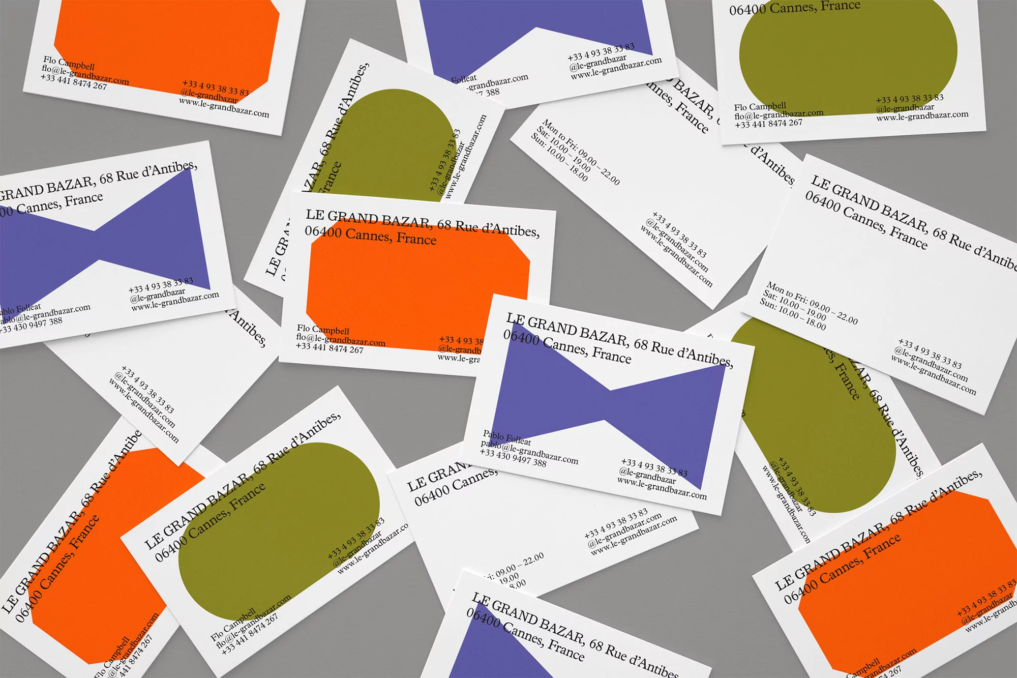 Scattered business cards for Le Grand Bazar in Cannes, France, featuring colorful geometric shapes and contact information on a gray surface.
