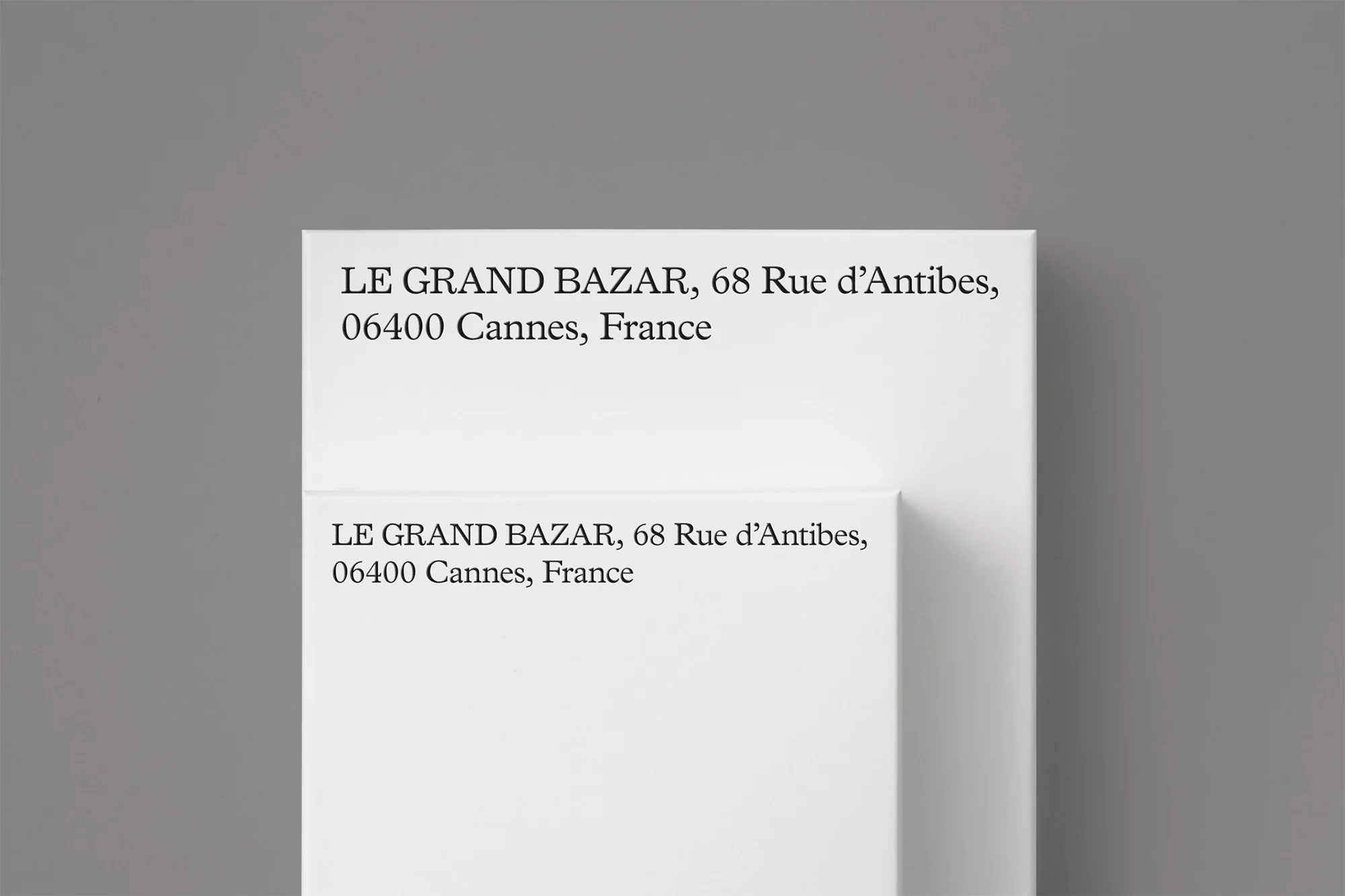 Close-up studio shot of two white cards featuring the text 'LE GRAND BAZAR, 68 Rue d'Antibes, 06400 Cannes, France' in black ink.