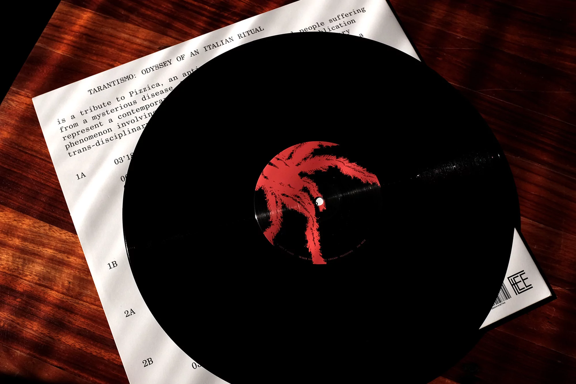 Overhead shot of a black vinyl record with red graphic on a white album cover on a dark wood surface. Music theme.