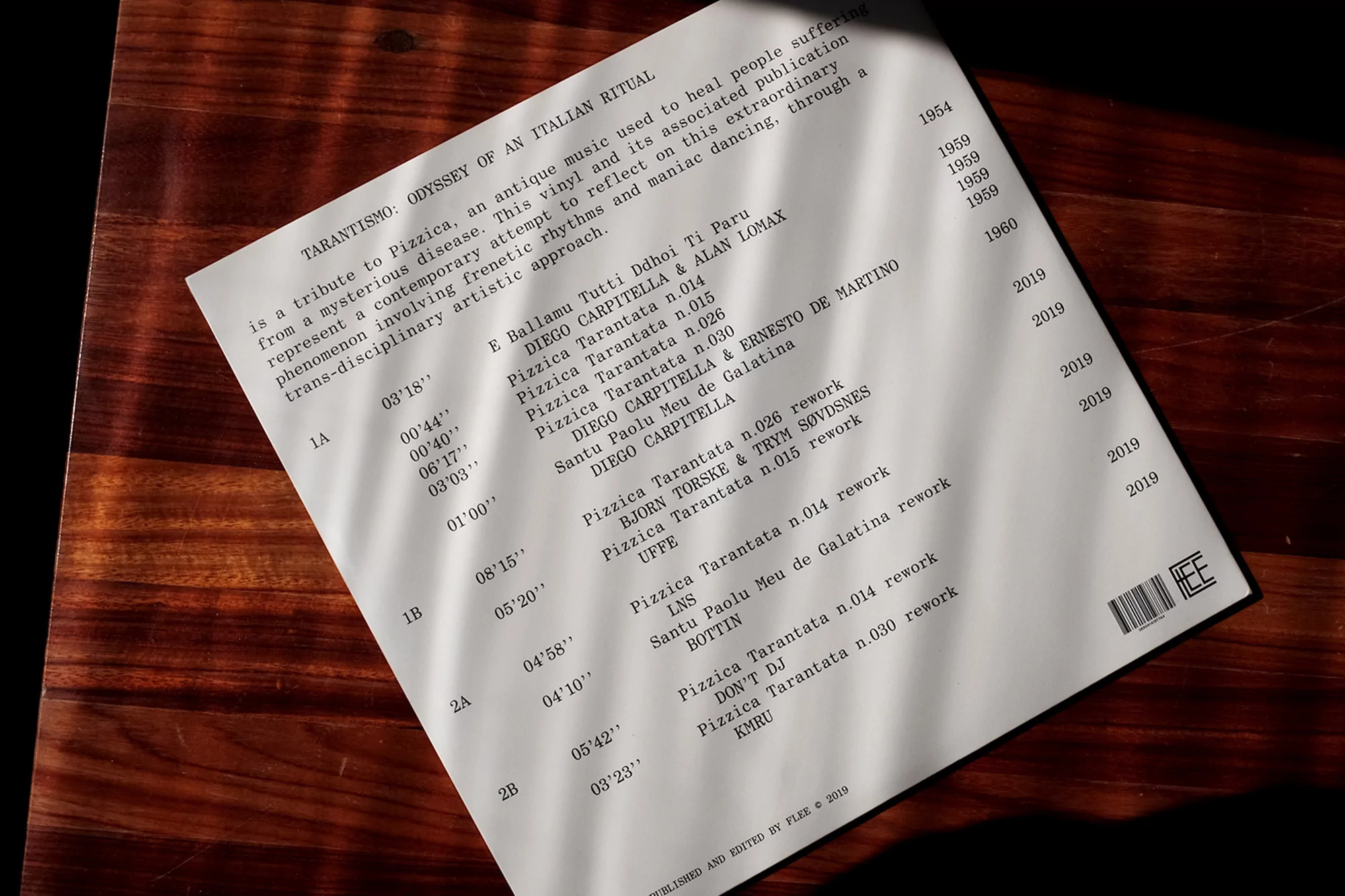 Text on a white page lists details for 'Tarantismo: Odyssey of an Italian Ritual'. Dark wood and shadows add contrast. 