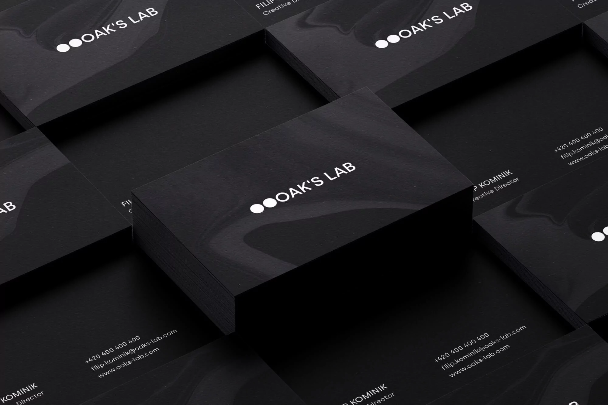 Close-up of several black business cards stacked; the company logo, OAK'S LAB, appears in white on the top cards.