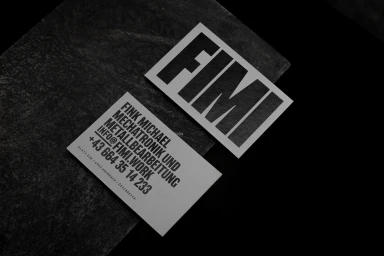 Two white business cards with bold black typography resting on a dark textured stone surface