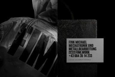 Monochrome brand identity design for FIMI featuring a hooded jacket with bold lettering and a business card on a textured surface.