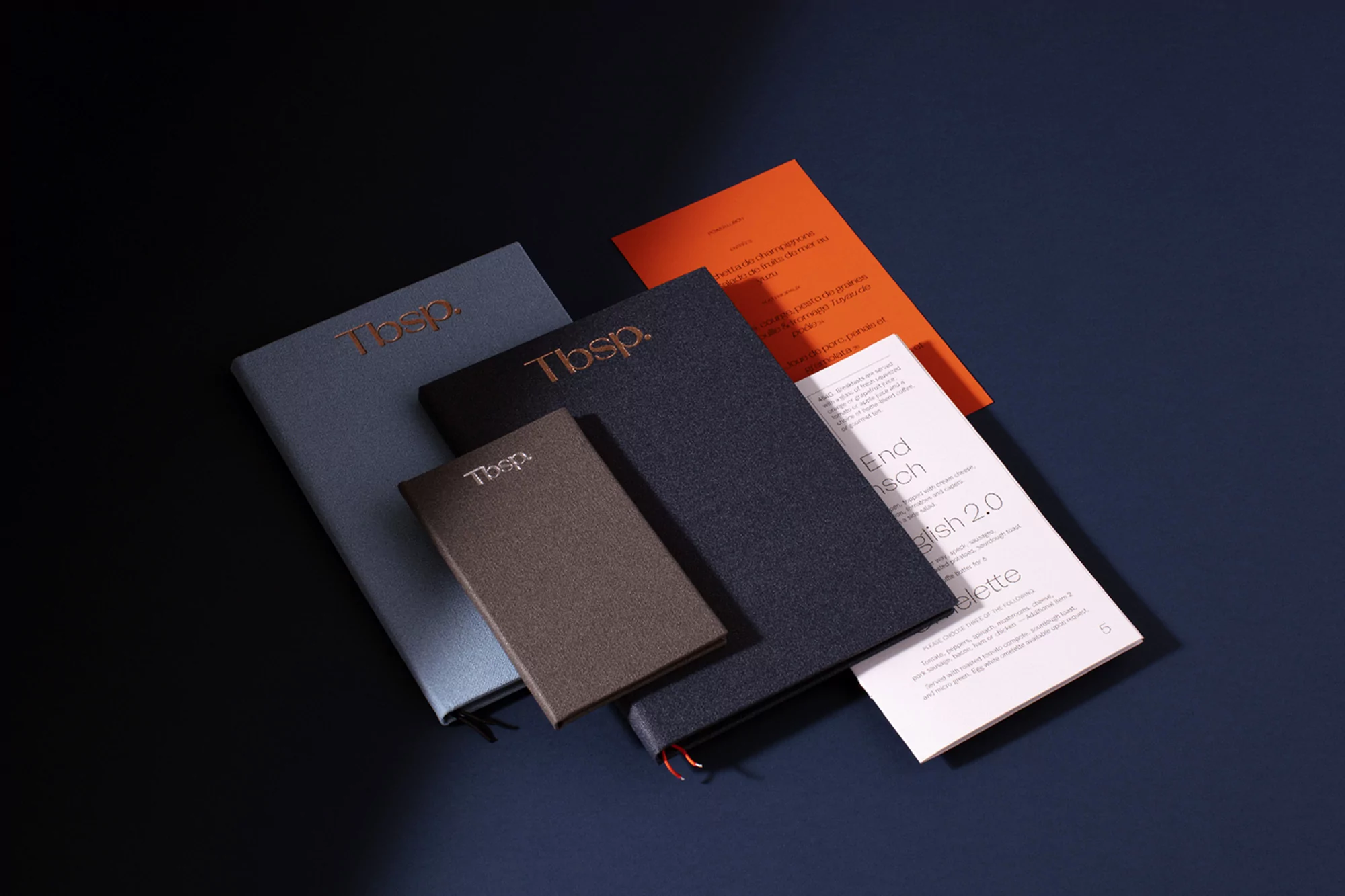 Several Tbsp brand notebooks and papers displayed on a dark blue surface, showcasing various sizes and colors of the stationery.