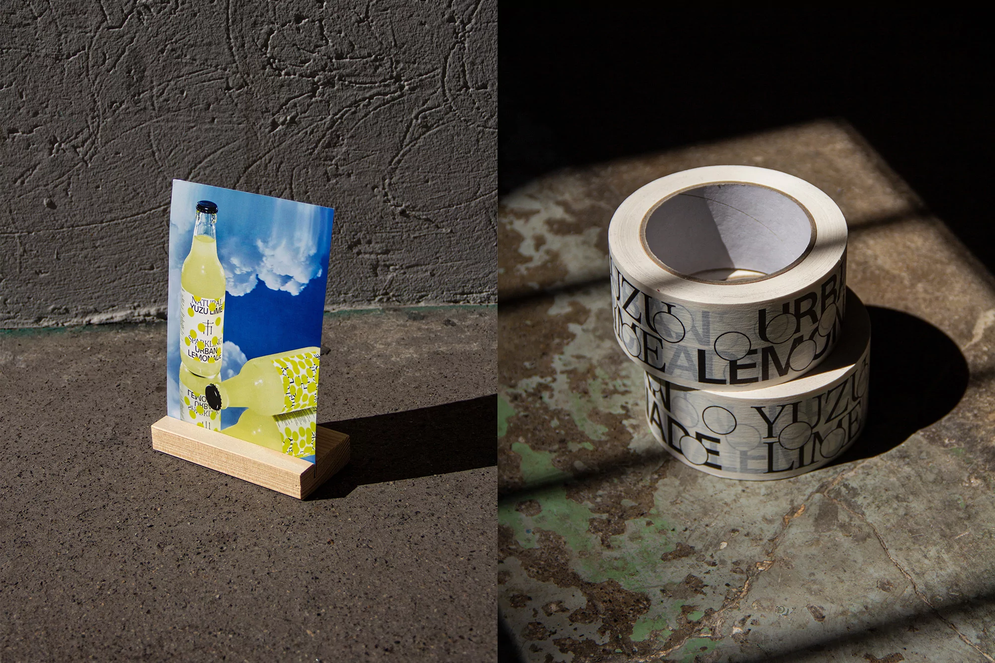 Studio shot of two rolls of tape and a postcard with a drink bottle on a wooden stand, set against a textured wall and floor.