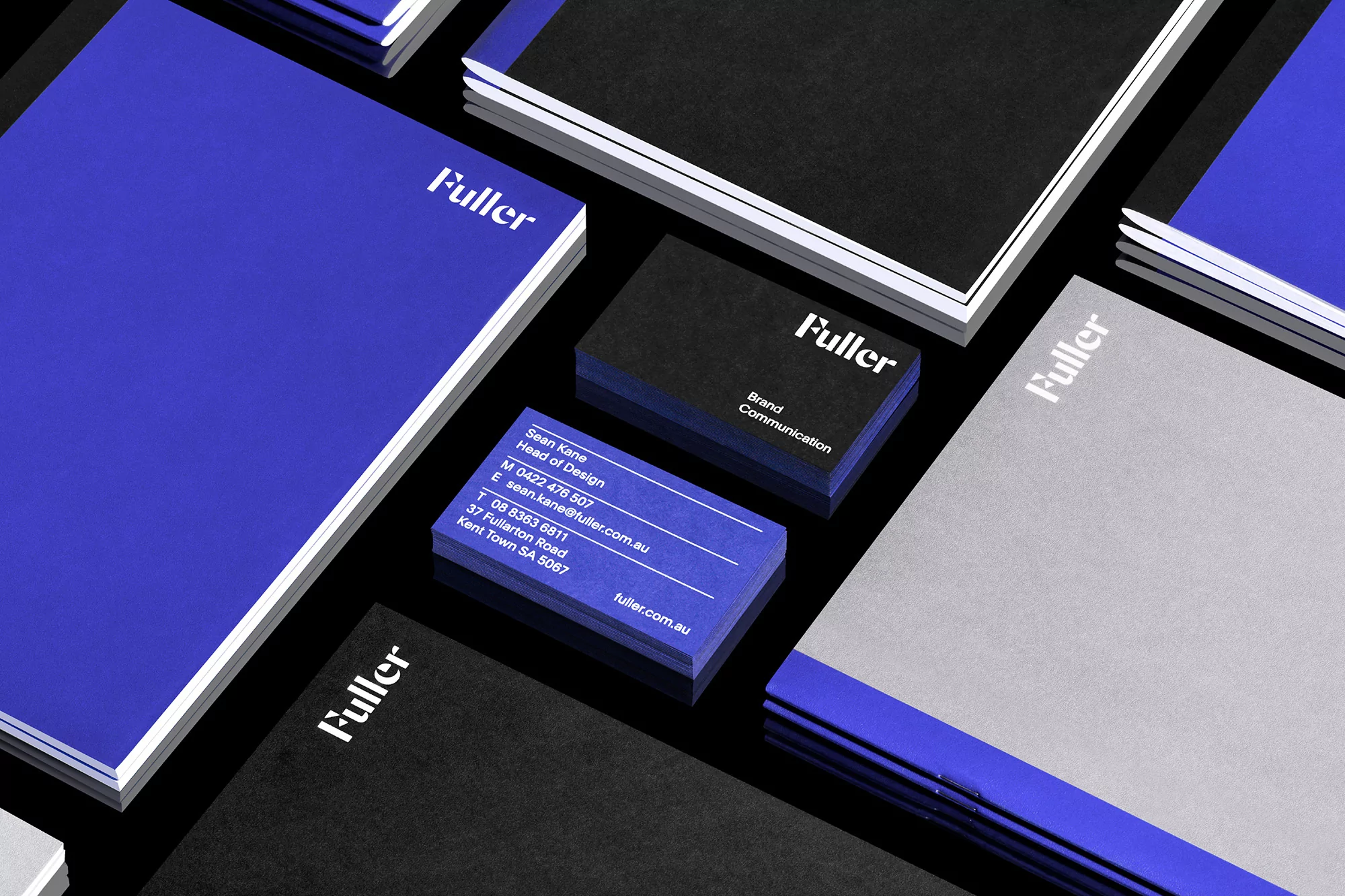 Corporate stationery featuring the wordmark 'Fuller' in white on blue, black, and grey, arranged on a black background with a high-angle view.