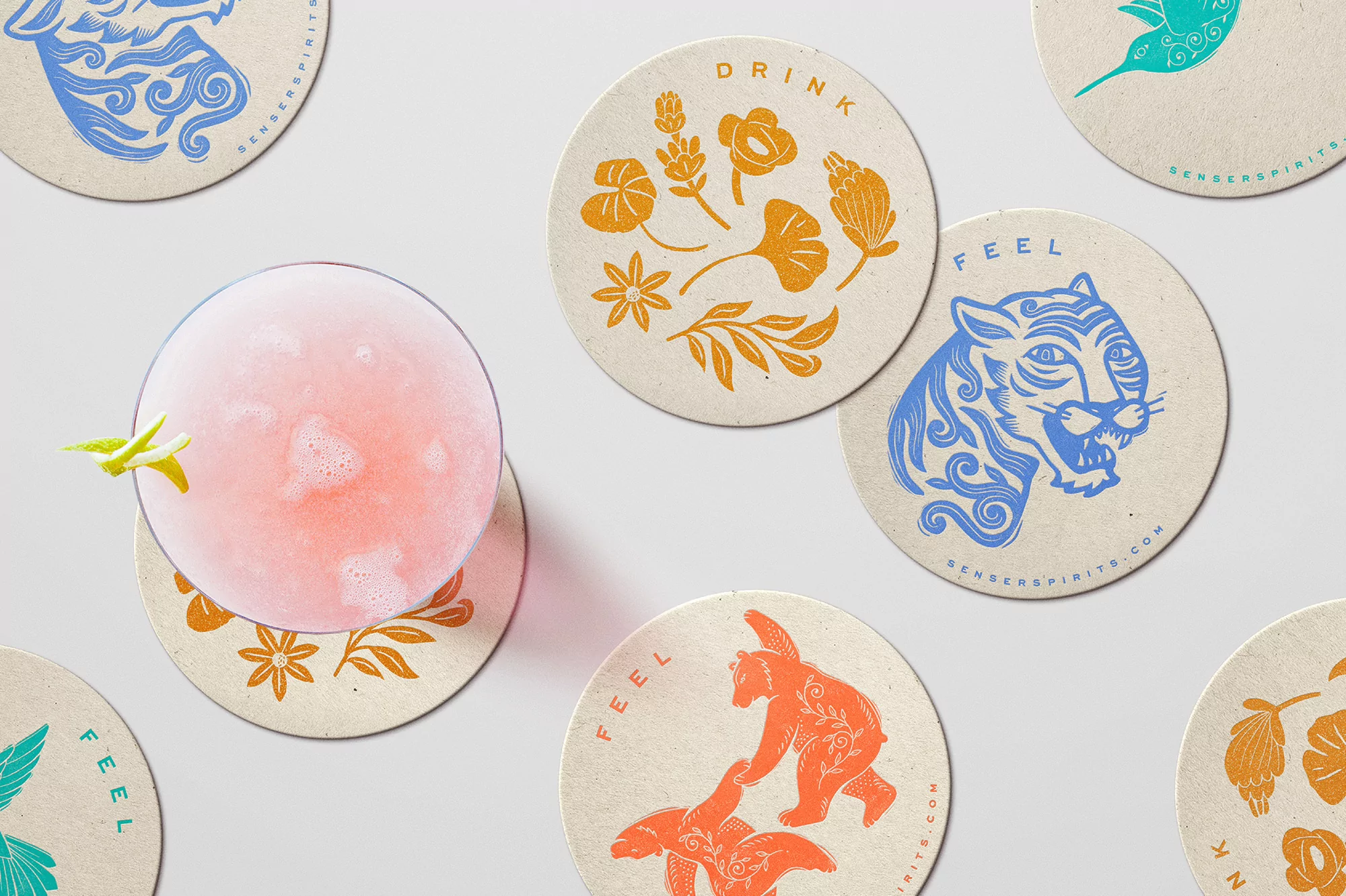 Overhead shot of a pink cocktail on a botanical-print coaster, surrounded by other coasters featuring animal and floral designs.