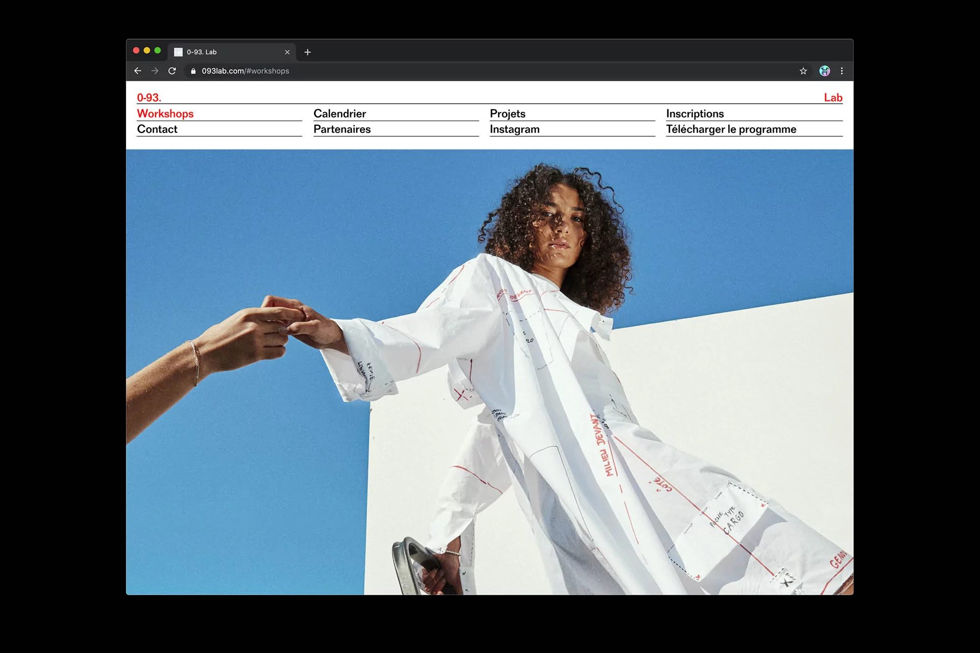 Fashionable woman in oversized print shirt with hands holding in the background, against blue sky, as shown on 0-93 Lab webpage.