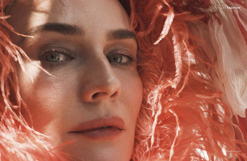 Close-up portrait of a fair-skinned adult woman with light eyes, surrounded by orange feathers, showcasing a beauty and fashion aesthetic.