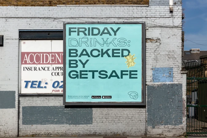 Outdoor billboard advertisement for GetSafe featuring a cracked phone graphic on a blue background on a brick wall in an urban setting.