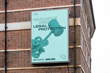 Outdoor billboard advertisement for Getsafe featuring a green legal protection poster mounted on a brick building exterior.