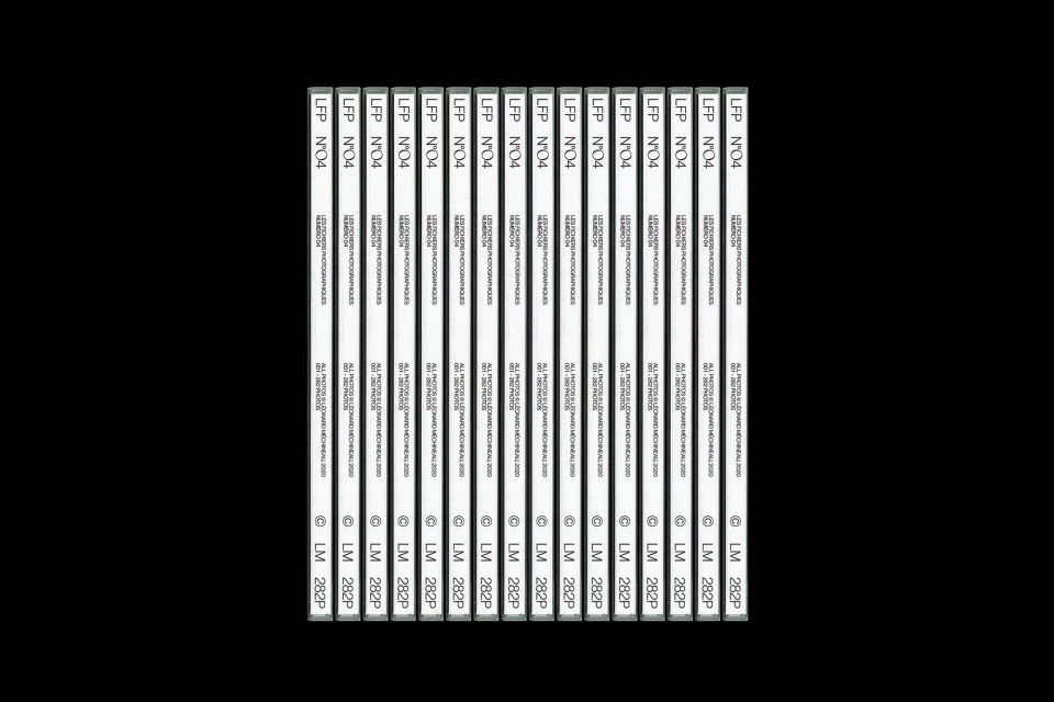Multiple identical white labeled cassettes are aligned in rows on a black background, creating a pattern effect with vintage media.