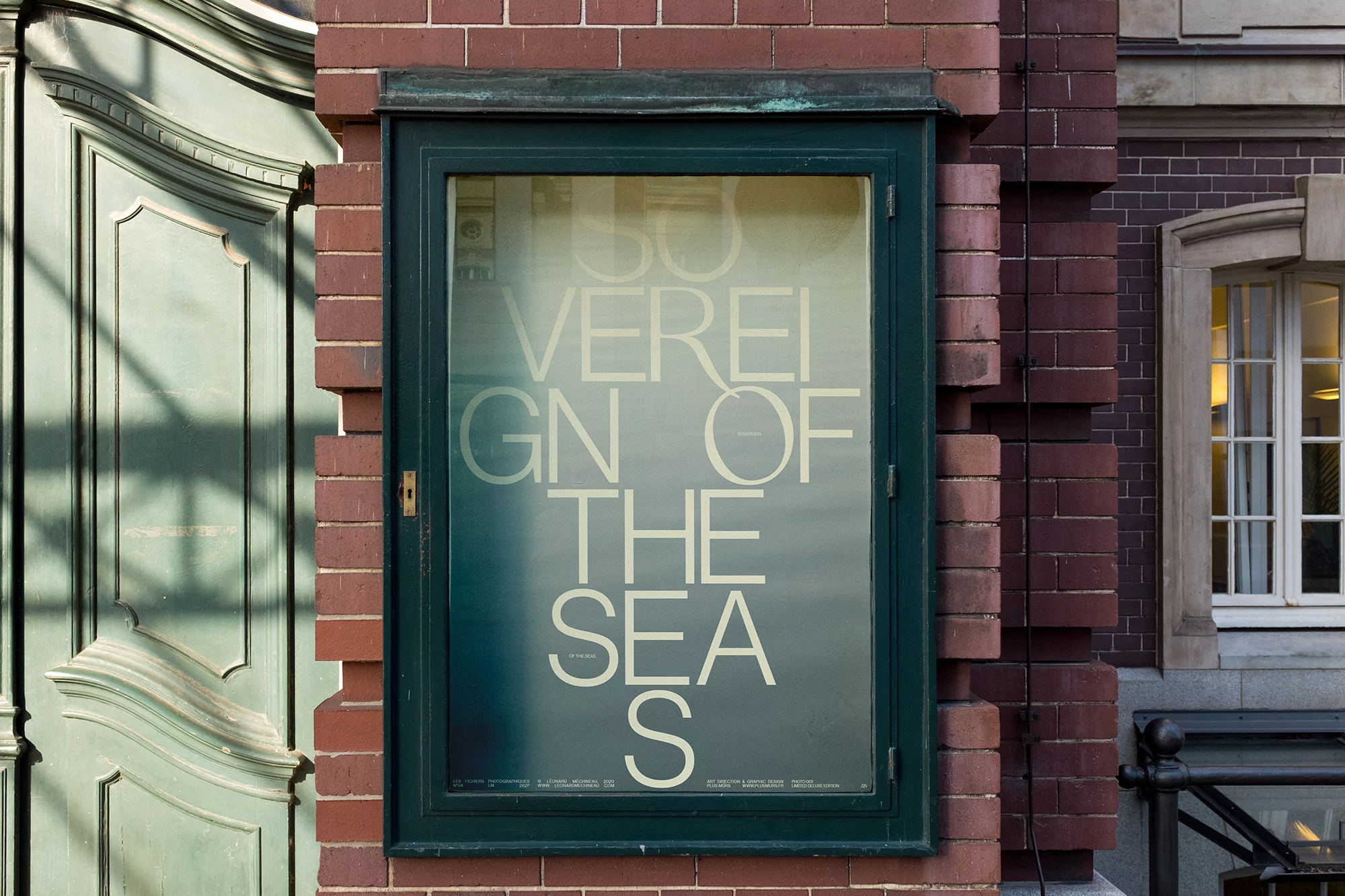Outdoor shot of a framed sign on a brick wall adjacent to a green door, featuring large white text that reads 'SOVEREIGN OF THE SEAS'.
