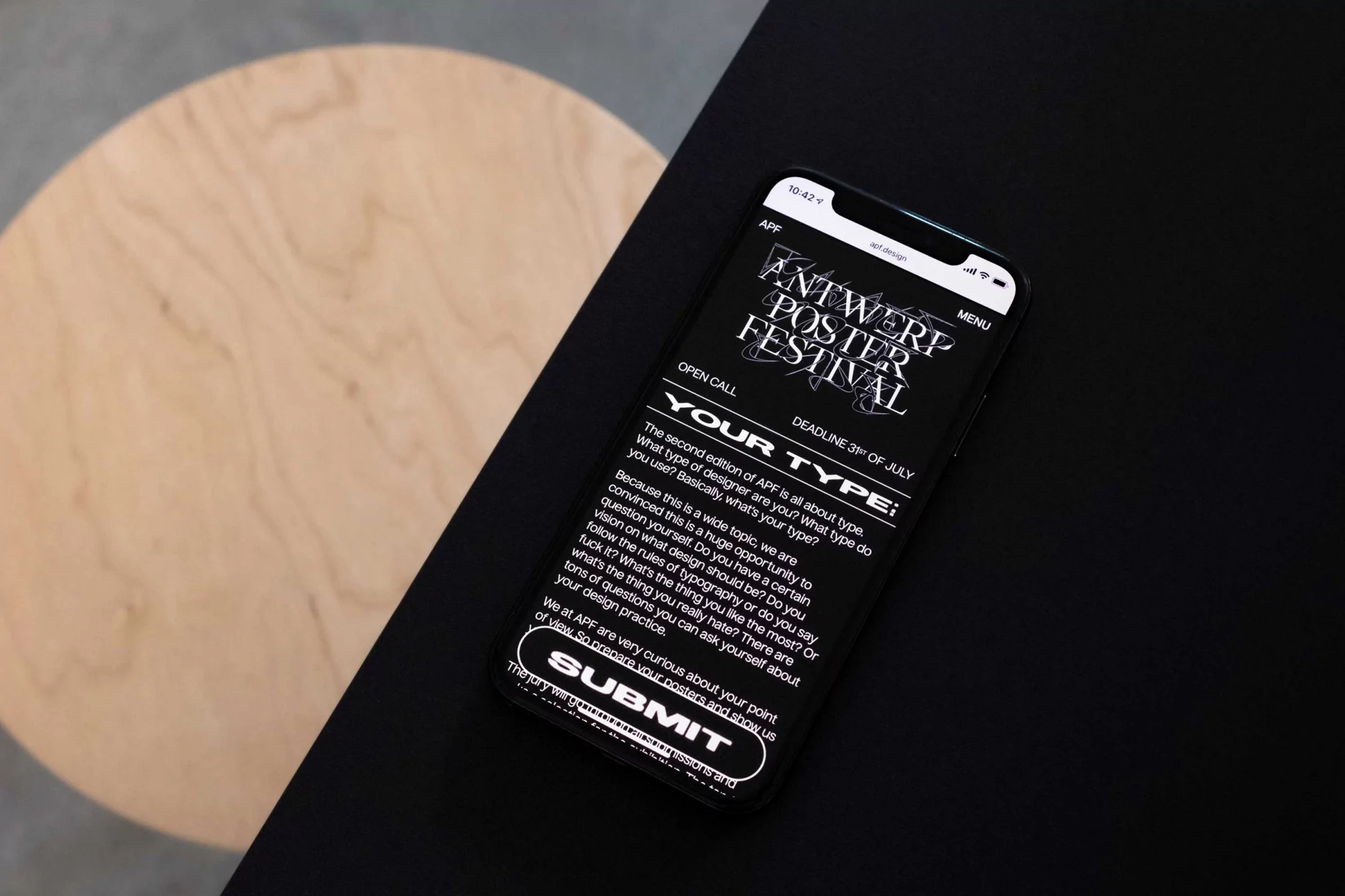 Smartphone on black surface displaying an Antwerp Poster Festival call for entries, showcasing typography and graphic design elements.