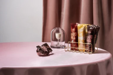 Packaged chocolate bars in a gold wire rack next to a small glass cloche on a table with a pink tablecloth