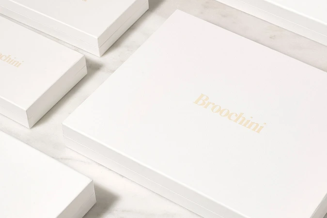 Several white presentation boxes with gold foil typography arranged neatly on a marble surface.