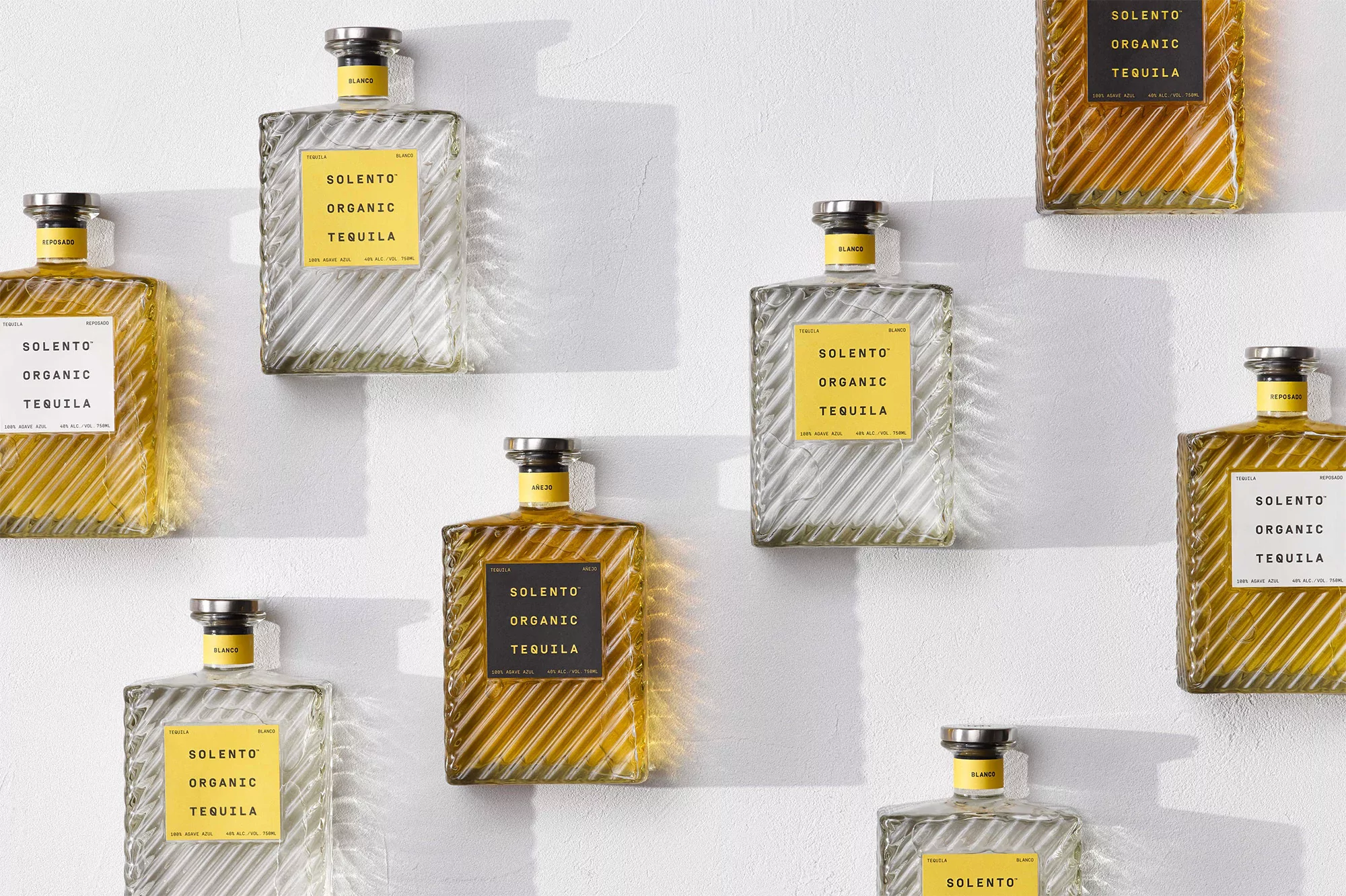 Several square glass bottles of Solento Organic Tequila arranged on a white surface, some filled with clear liquid and others with amber liquid.