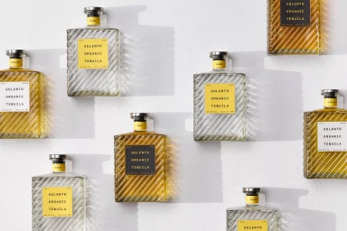 Multiple rectangular glass bottles of Solento Organic Tequila arranged on a textured white surface under direct sunlight