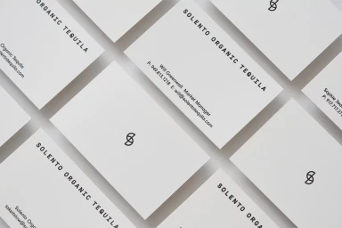 Multiple white business cards with black typography arranged in a repeating diagonal pattern on a white surface.