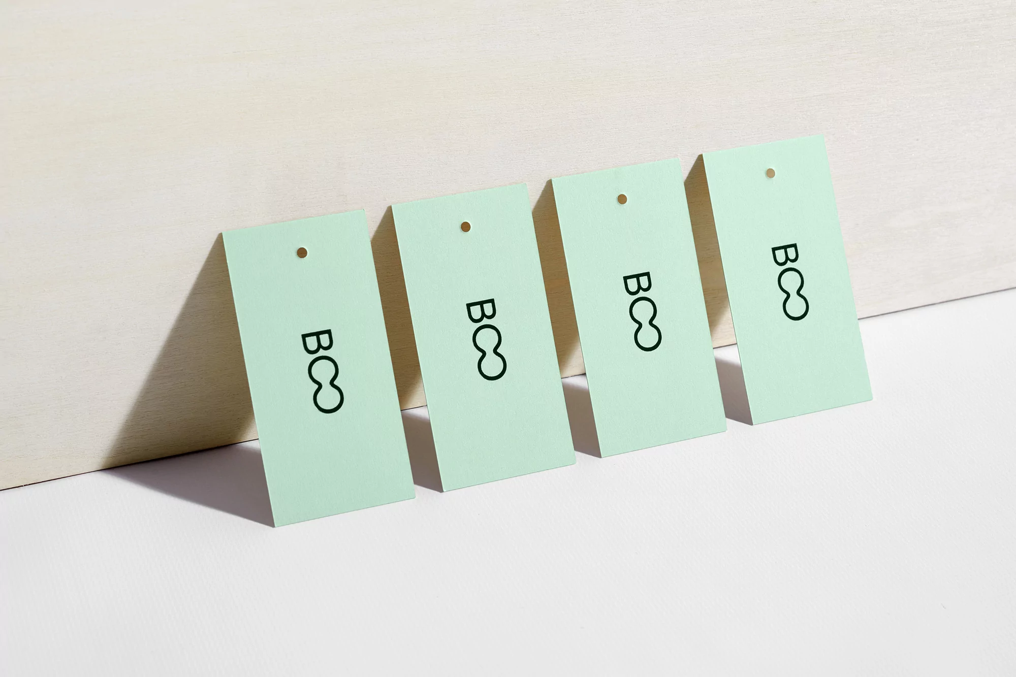 Four light green tags with the letters BCO in black text are aligned diagonally on a light beige background, providing a clean, minimal aesthetic.