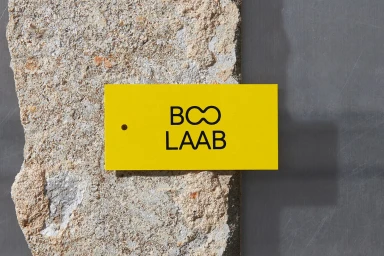 Bright yellow rectangular brand label featuring black BOO LAAB text against a rough stone and grey metal background