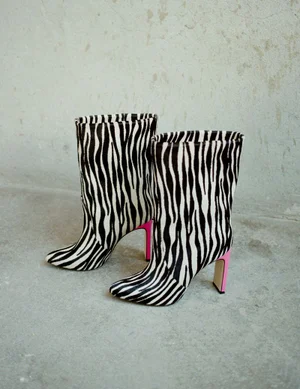 Pair of zebra print boots with pink heels placed on a grey concrete floor against a textured wall.