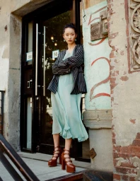 Model Jiwon Christine Ra wearing a striped blazer and mint green dress leaning against a doorway for L'Officiel Baltics Revival