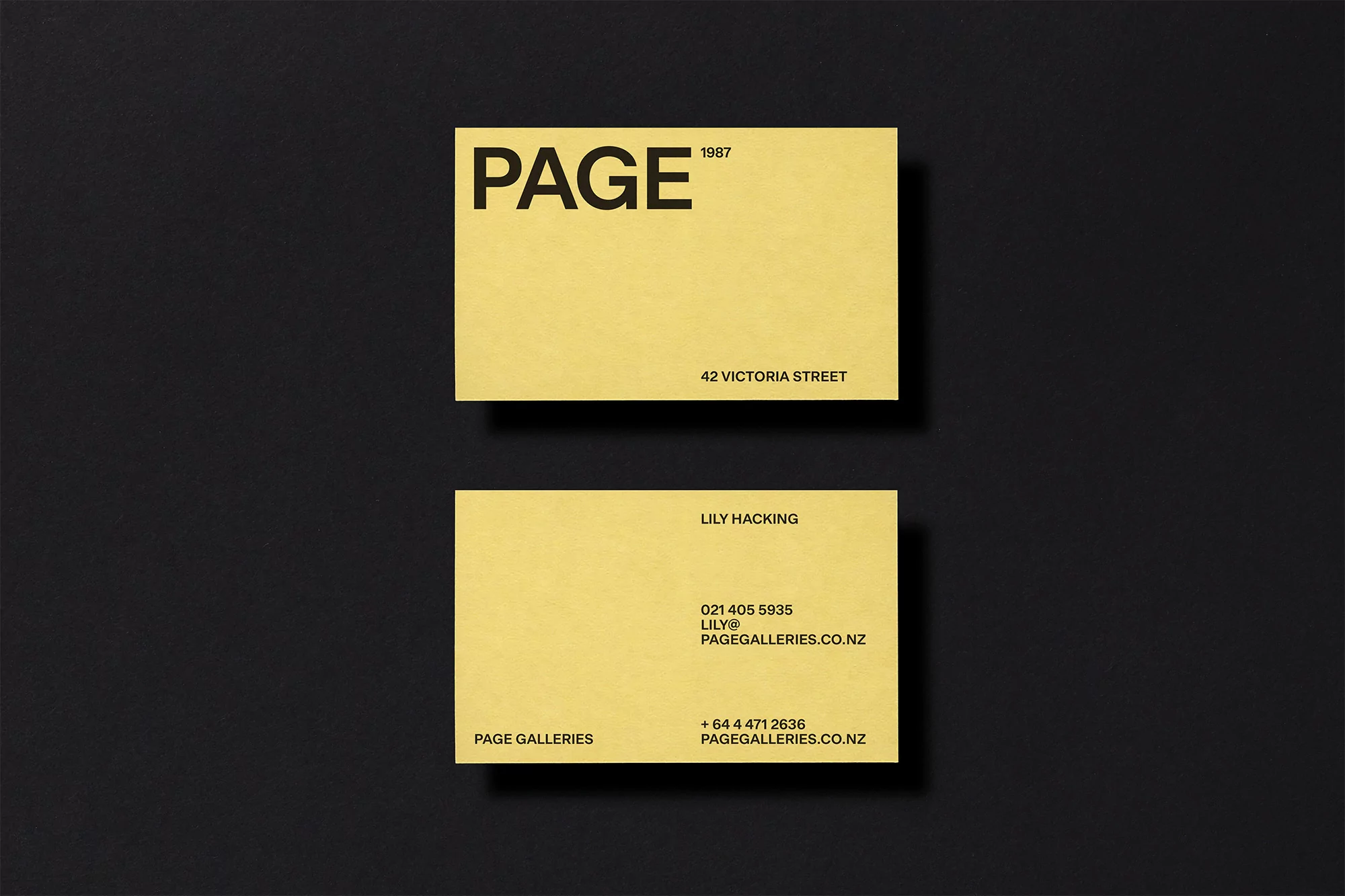 Two yellow business cards with black text, arranged on a black background. Simple design, studio shot, clean corporate aesthetic.