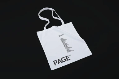 White canvas tote bag with black typographic branding lying flat on a solid black background.