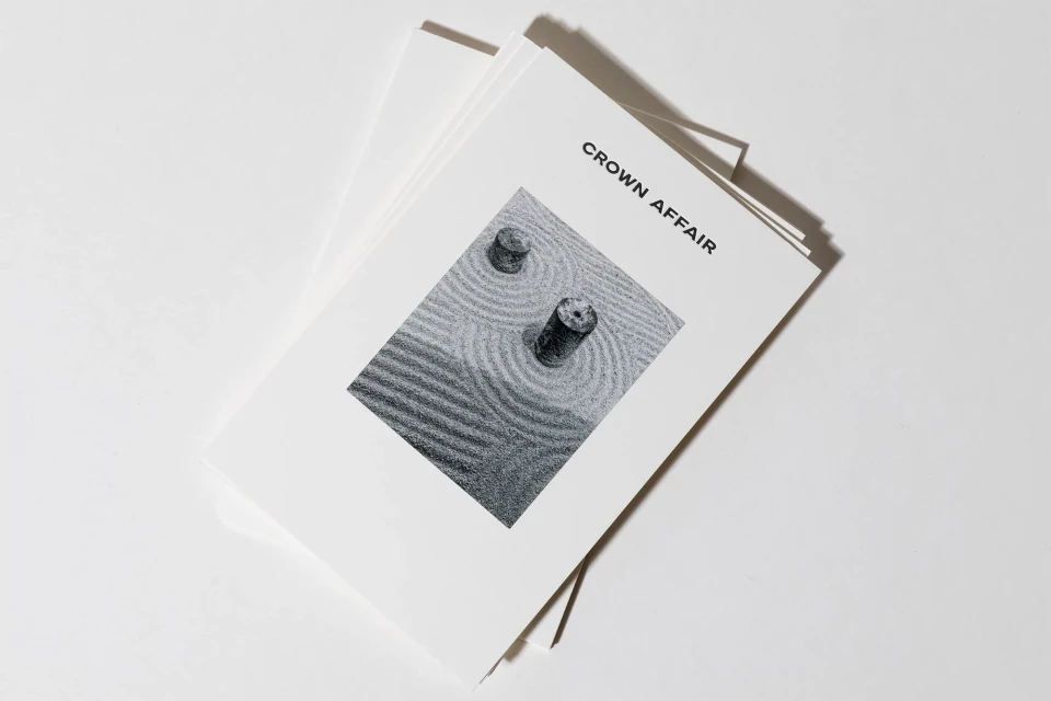 Stack of white paper documents, one featuring a black and white minimalist zen garden image with concentric circles and two cylinders.