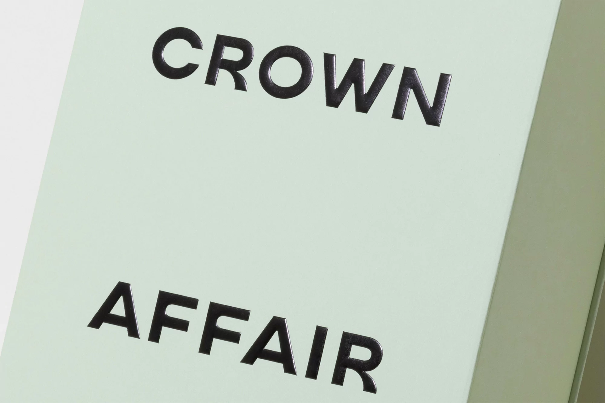 Close-up of black text 'Crown Affair' on a light green surface, providing a clean and modern aesthetic for design or product imagery.
