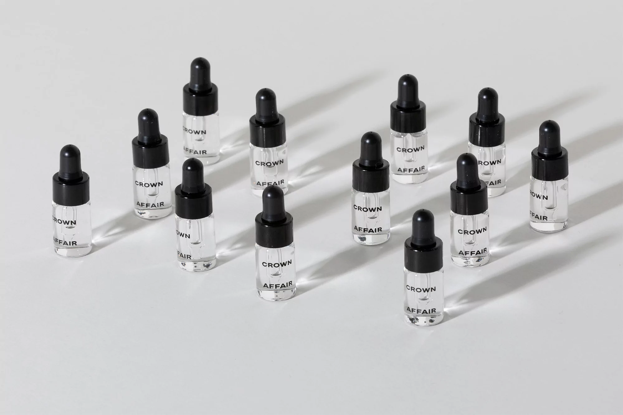Collection of clear glass bottles with black dropper caps arranged neatly on a white surface, showcasing minimalistic product presentation.