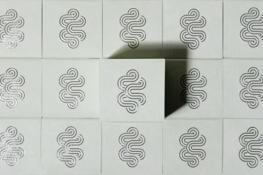Close-up photograph of repeating white packaging squares featuring silver embossed labyrinth logos by Crown Affair.