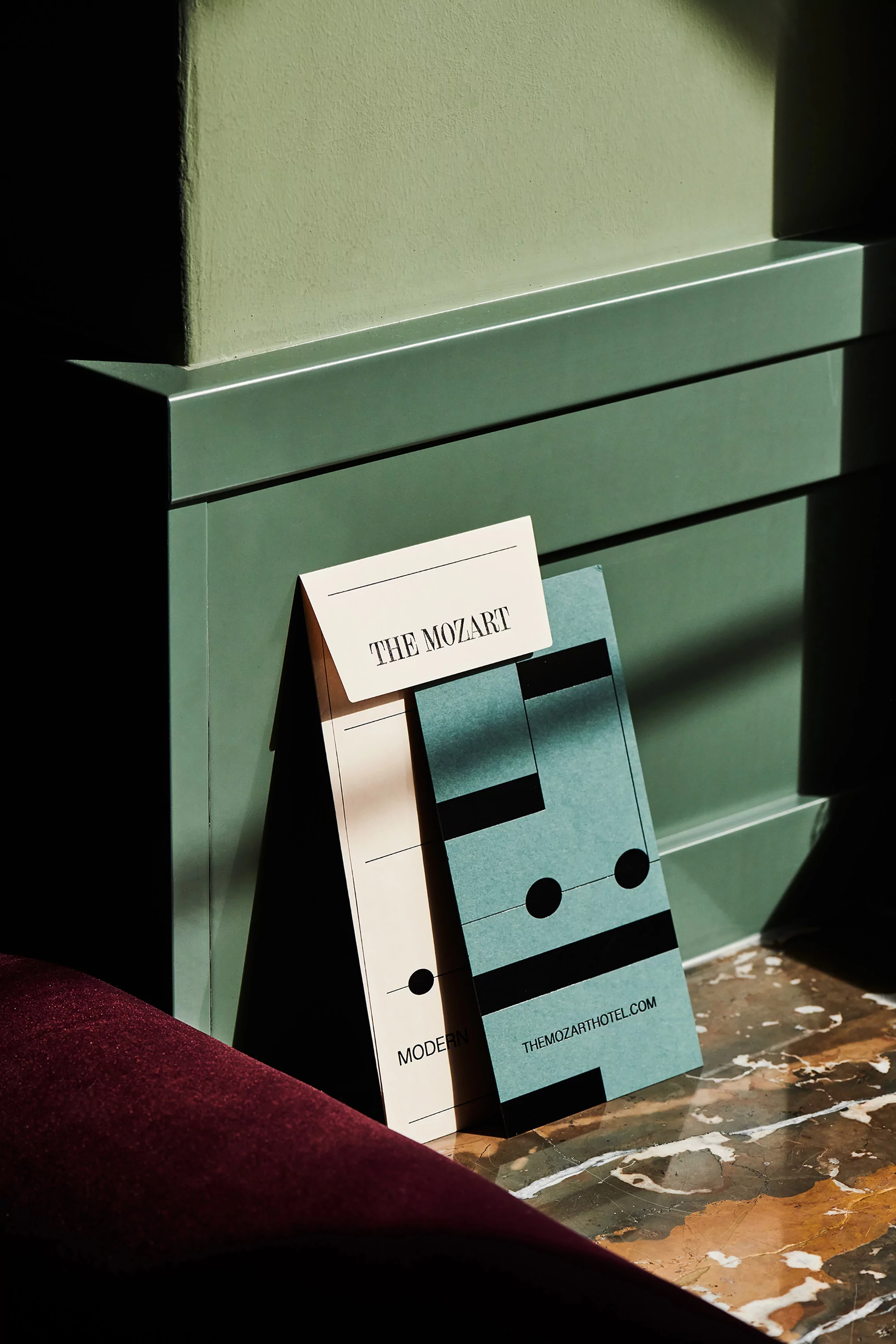 Promotional materials including business cards for The Mozart hotel, styled on a marble floor with green panelling in the background.