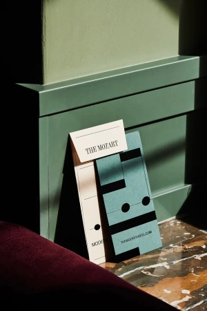 Promotional materials including business cards for The Mozart hotel, styled on a marble floor with green panelling in the background.