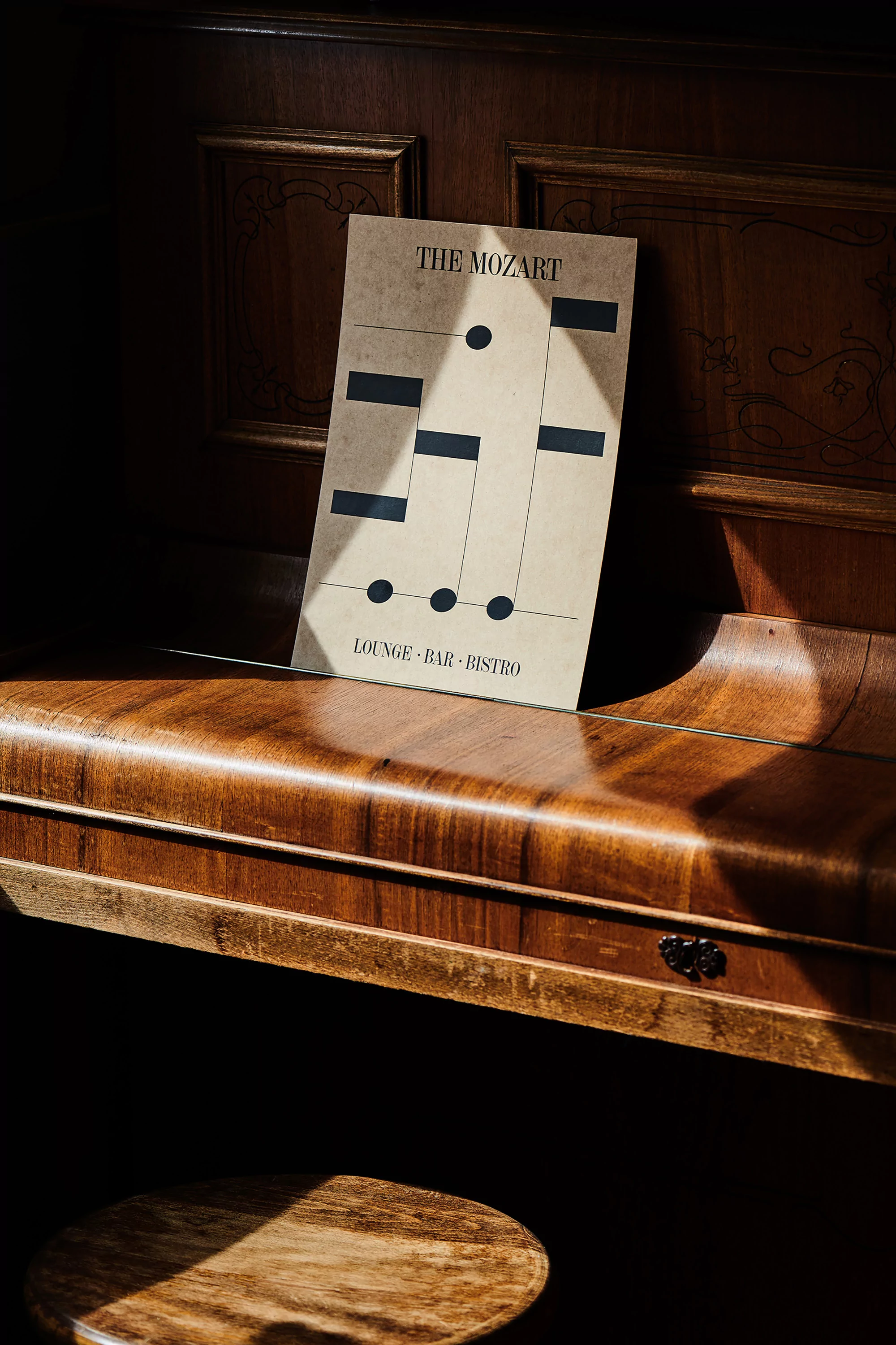 Sheet music for The Mozart lounge, bar and bistro rests atop a wood piano, illuminated by a beam of natural light in an indoor setting.