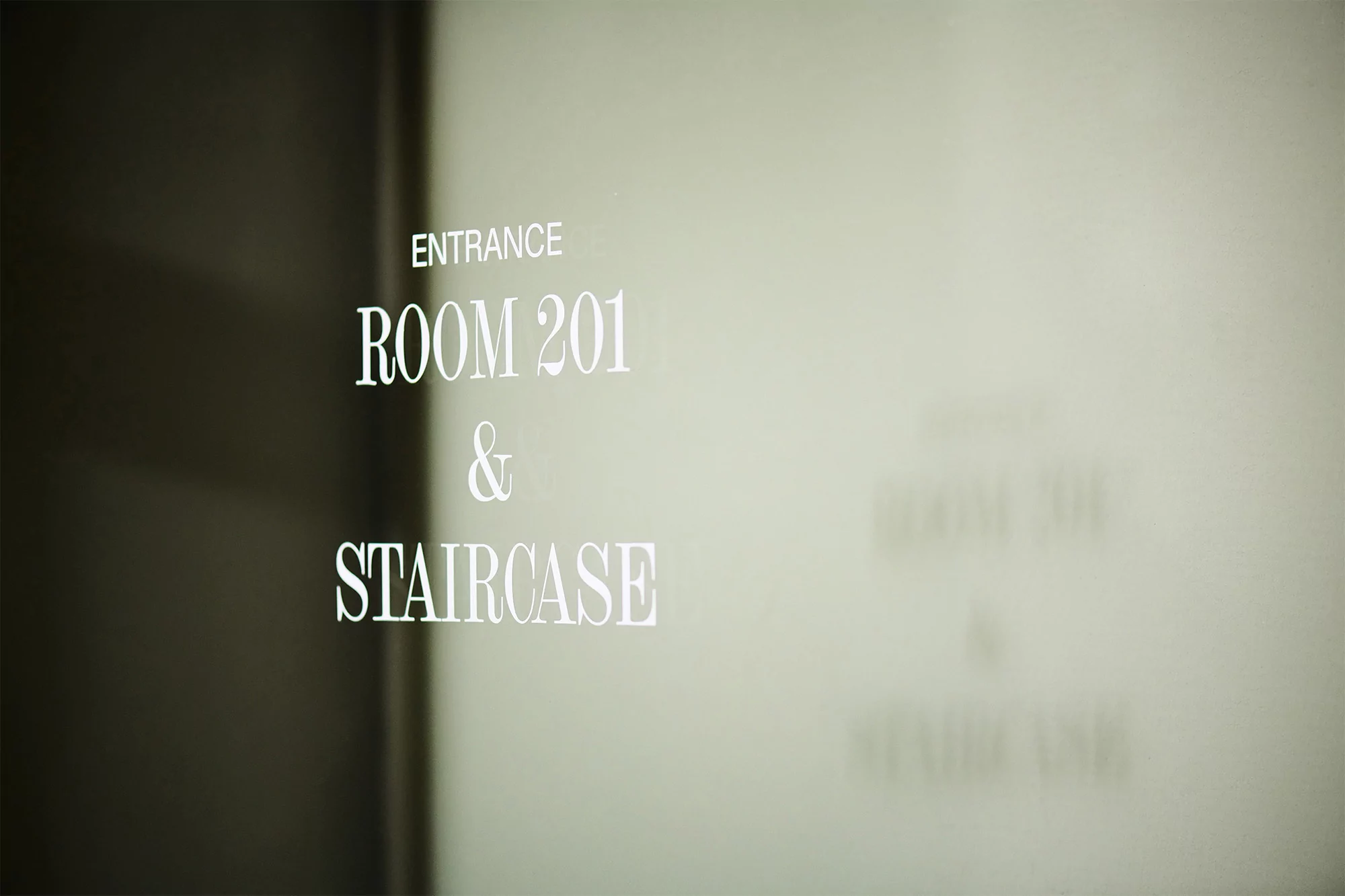 Close-up of a sign reading 'Entrance, Room 201 & Staircase' in a minimalistic interior, promoting building navigation and accessibility.