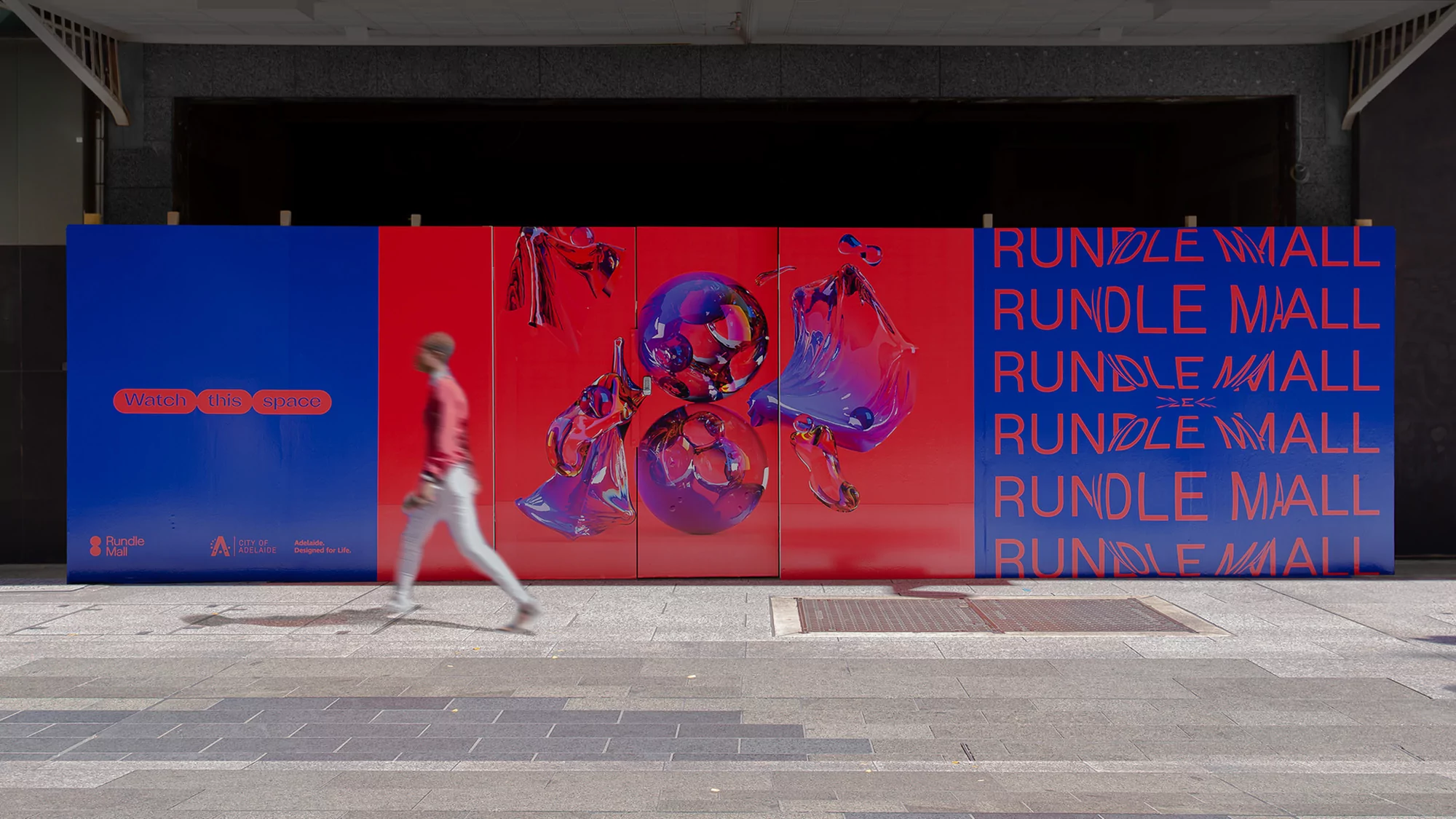 Sidewalk view of person walking past Rundle Mall hoarding with abstract art and lettering in red, white, and blue in an urban setting.