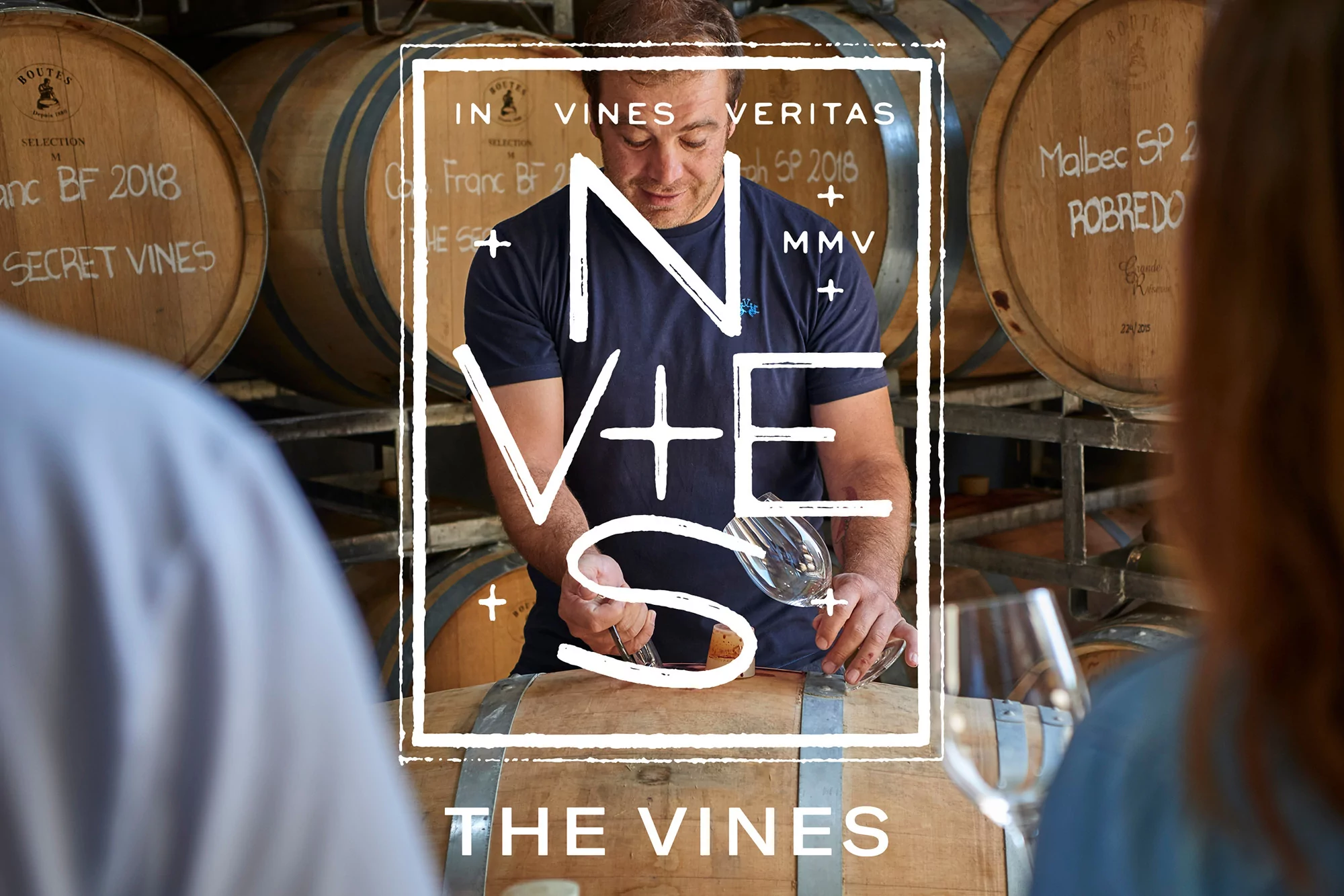 Man in navy shirt sampling wine in a barrel room, with wine barrels in the background and text overlay on the image.