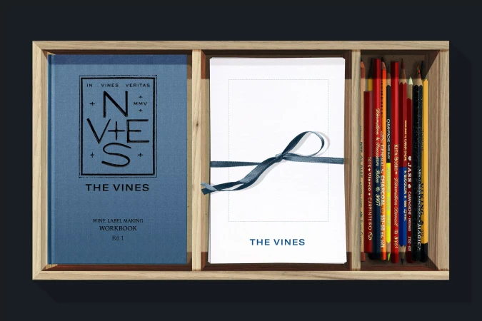 Elevated studio shot of a wooden box set with a blue workbook, white paper, colored pencils, and a blue ribbon.