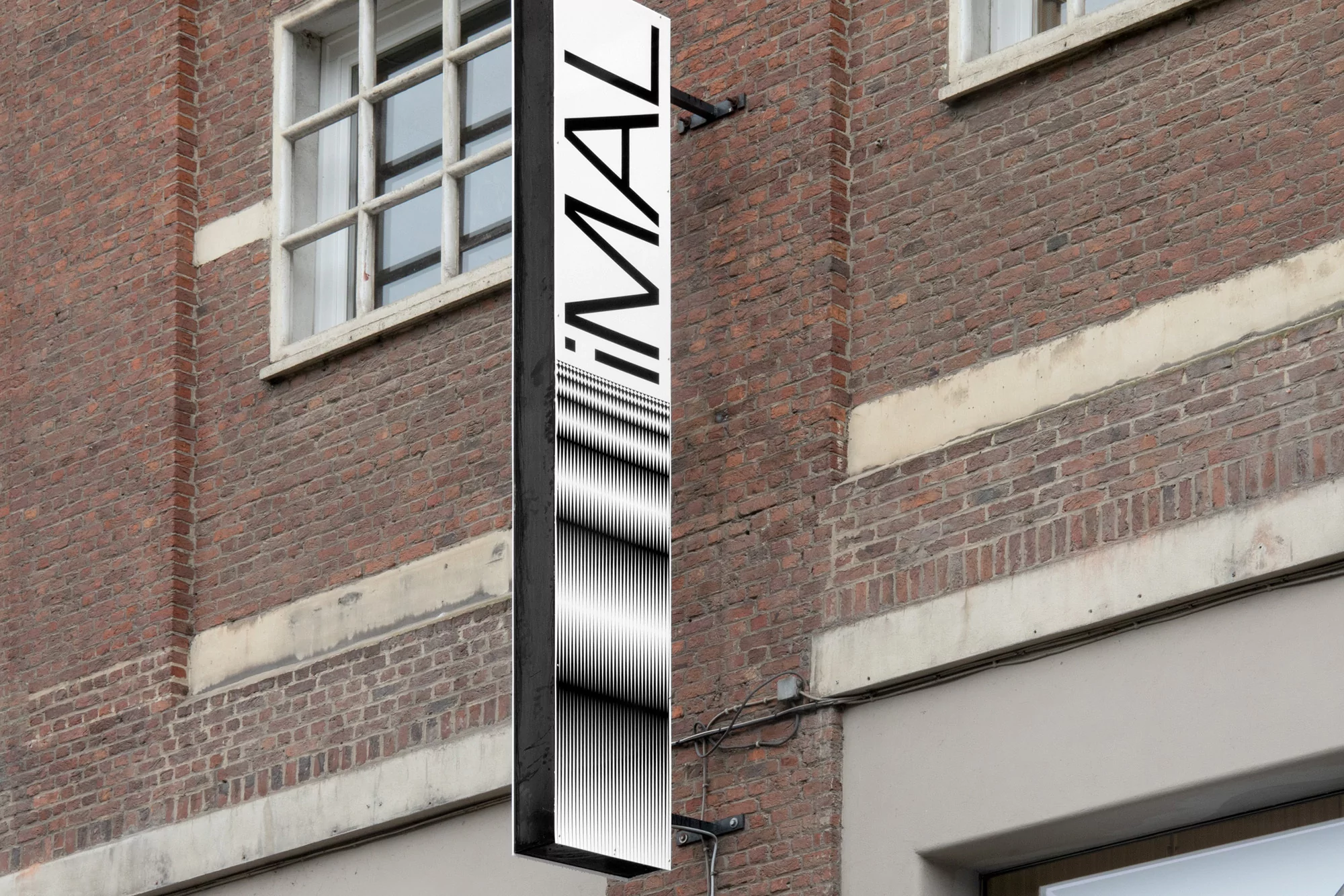 Outdoor business signage attached to a red brick building features bold text and a black and white abstract graphic design.