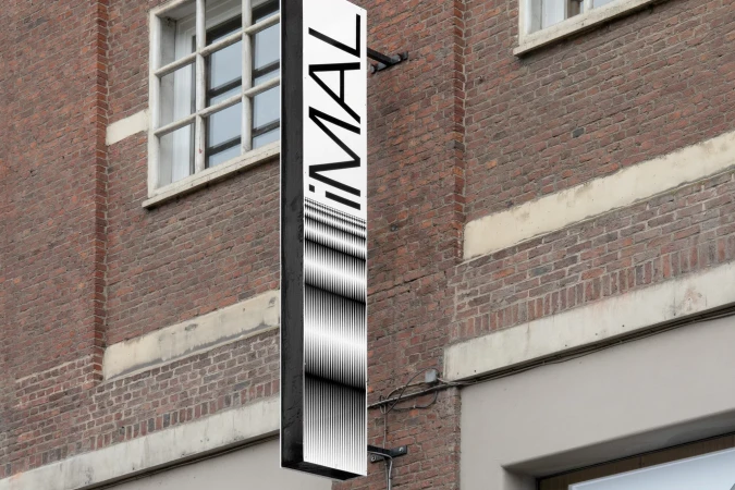 Outdoor business signage attached to a red brick building features bold text and a black and white abstract graphic design.