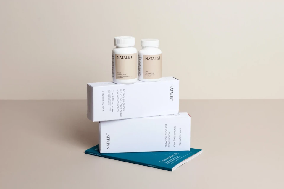 Natalist branded fertility products including pregnancy tests and supplements in white packaging on a light-beige surface.